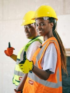 Two smiling construction workers in PPE gear posing with thumbs up.