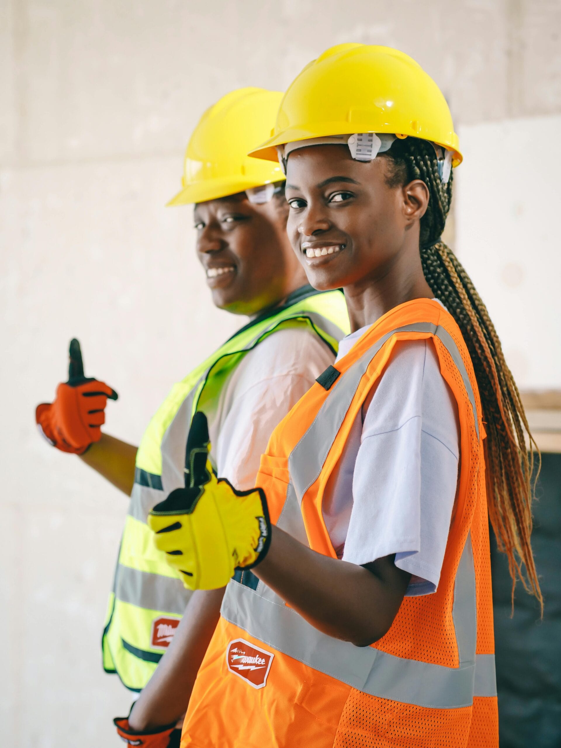 Two smiling construction workers in PPE gear posing with thumbs up.