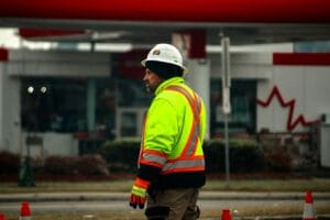 A construction worker wearing high-visibility gear and a helmet at a roadside in Canada.