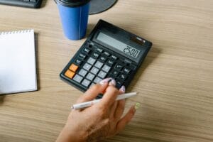 A person uses a calculator and pen on a wooden surface, focusing on office work.